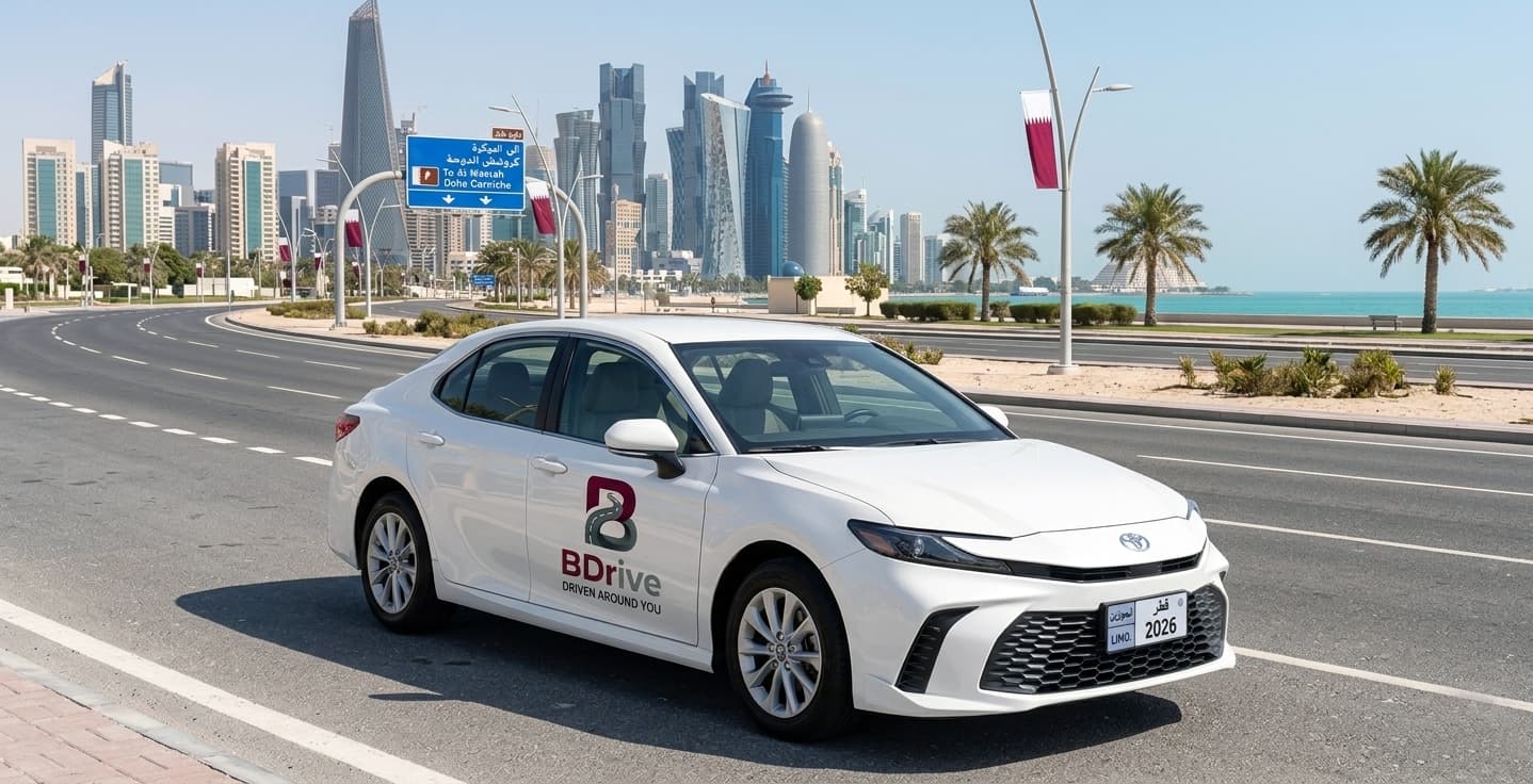 BDrive branded white Toyota Camry driving on Doha Corniche with the Qatar skyline, Doha Financial District towers, Qatar flags, and the Arabian Gulf in the background